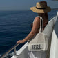 Woman on a boat wearing a 'Bride' bag and straw hat, looking at the ocean.